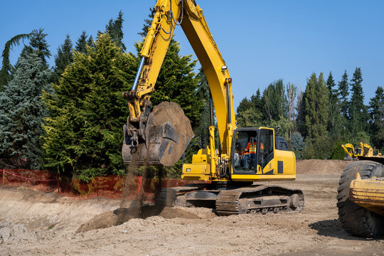 Large excavator with bucket full of dirt, spilling some of the soil with moving it, earthworks construction project site on a sunny day
 - Powered by Adobe