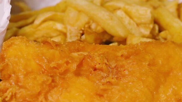 Slow Moving Camera View Over Traditional British Fish and Chips Meal in Takeaway White Paper. Deep Fried Fresh Cod Seafood Served in Britain.