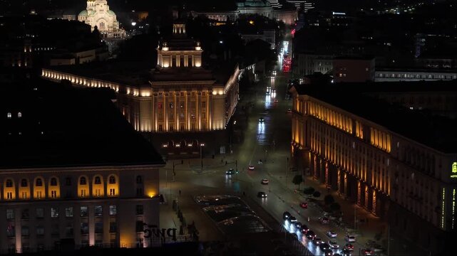 Night drone capture of Sofia&rsquo;s city center featuring the Bulgarian National Assembly, the illuminated Alexander Nevsky Cathedral, and surrounding glowing buildings.
