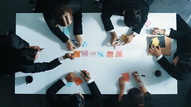 Top down aerial view of diverse business people writing marketing idea or taking a note on sticky notes. Professional executive manager group brainstorm financial plan at meeting room. Directorate.