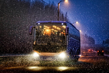 Blue bus driving on highway in heavy snowfall on a dark winter night. 