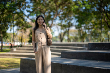 Fototapeta premium Young woman walking and talking on phone in park