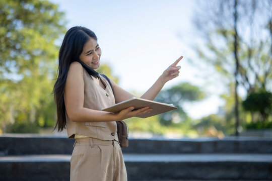 Asian businesswoman multitasking, talking on phone, pointing outdoors