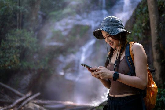 Woman hiking using smartphone at waterfall in forest