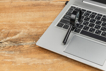 Magnifying glass resting on a laptop keyboard at a wooden table