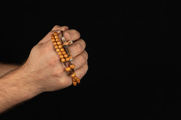 Hands holding wooden prayer beads against a black background