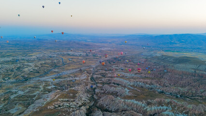 Goreme, Nevsehir, Turkey. Massive fleet of hot air balloons with fire bursts flying over Cappadocia plateau and valleys in clear morning with blue haze at sunrise. Aerial View
