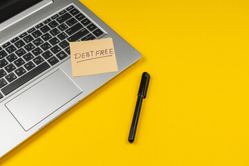 Note on a laptop reminding to stay debt free on a bright yellow background