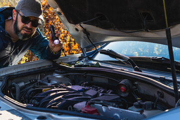 Man inspecting car engine with flashlight in outdoor setting