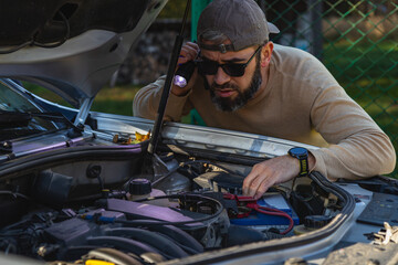 Man repairs car engine in backyard during sunny day