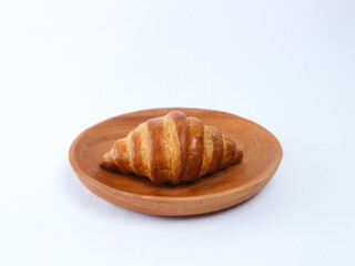 Golden brown croissant on a wooden plate isolated on a clean white background; simple food styling, bakery pastry photography
