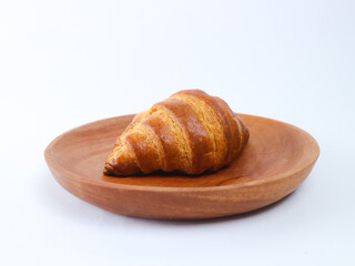 Golden brown croissant on a wooden plate isolated on a clean white background; simple food styling, bakery pastry photography