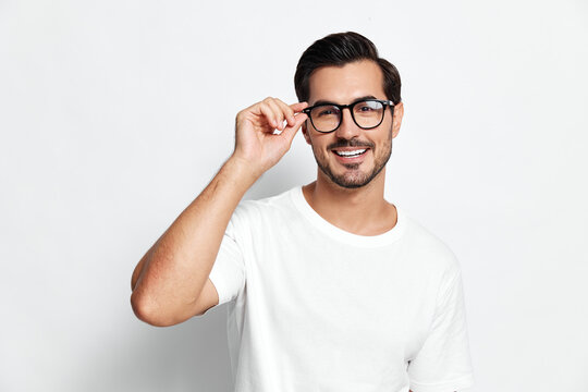 Smiling young man wearing glasses and a casual white t-shirt, posing confidently with a friendly expression against a solid light background.