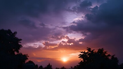 Dramatic sunset sky with vibrant purple and orange clouds over silhouetted trees