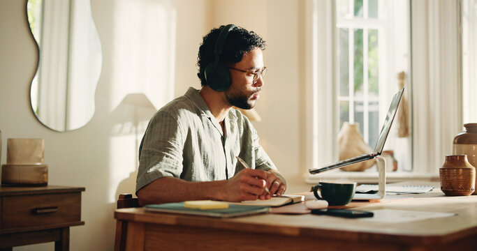 Laptop, video call and man with headphones, home and notes for logo design, listening and freelance. Creative, graphic designer and person with notebook for virtual meeting, writing and communication