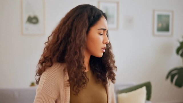 Young woman with curly hair coughing into her elbow indoors in a well-lit room, demonstrating proper respiratory etiquette to prevent germ spread during illness