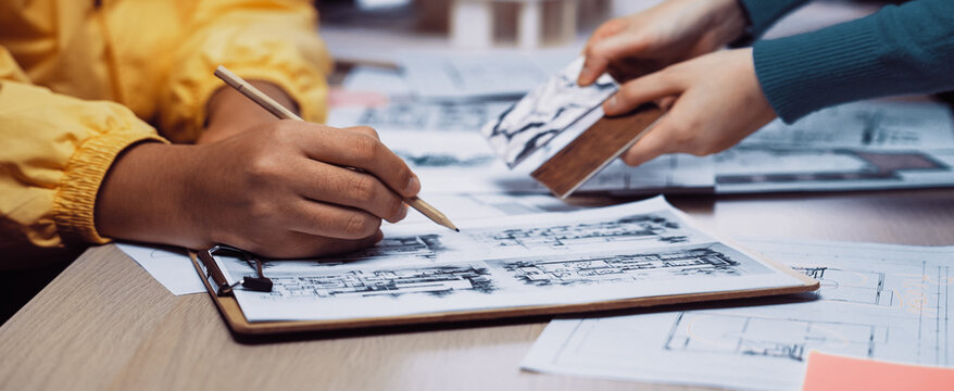 A dynamic scene showcasing a team engaged in a design session, where hands collaborate on sketches and models amidst architectural plans and creative discussions. SACTR - Powered by Adobe