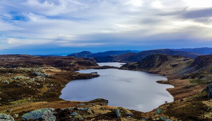 Scenic View of a Serene Lake Surrounded by Rugged Mountain Landscape under a Cloudy Sky