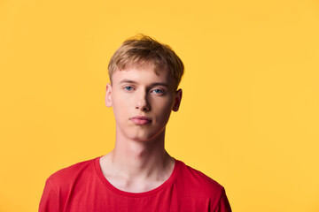 Young man in a red shirt stands against a bold yellow backdrop, showcasing contemporary casual...