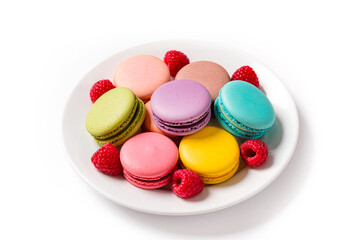 Colorful french macarons with fresh raspberries on white plate isolated on white background. Sweet almond cookies with berry fruit for dessert, bakery or pastry shop concept.