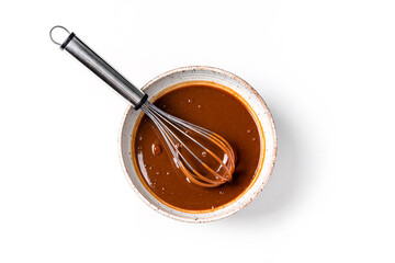 Top view of melted chocolate or cocoa batter in ceramic bowl with metal whisk isolated on white background. Process of preparing sweet baking cream or sauce.