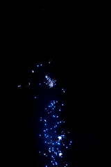 Sweeping blue firework plume bending across the sky, scattering bright star clusters that curl upward like a luminous wave of starlight rolling through the tranquil midnight air

