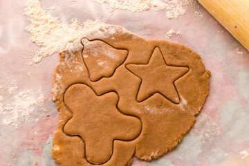 Homemade Christmas cookie preparation with dough, flour, cookie cutters and festive decorations on a kitchen table. Holiday baking process with ingredients and gingerbread shapes.
