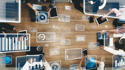 Team members engaged in a collaborative technology meeting surrounded by laptops and tablets, showcasing dynamic data visualizations for enhanced productivity and innovation. Xenic