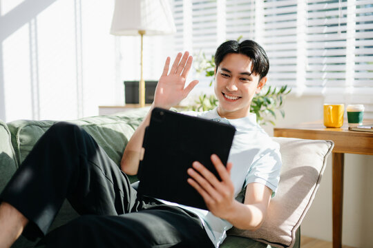 Young man on the phone, enjoying a relaxed moment at home with his smartphone, coffee mug, and modern living room