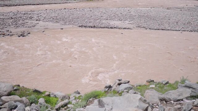 Slow motion shot of flooded Chenab river flowing in the mountains during the monsoon season after heavy rainfall as seen from Tandi village in Lahaul and Spiti district, Himachal Pradesh, India.