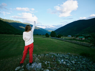 Obraz premium Woman standing on a rocky overlook in open countryside, arms raised toward distant mountains and valley, clear blue sky, vibrant landscape, feeling freedom and exploration