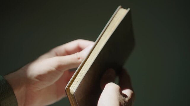 Hands hold and examine an old book in soft lighting, nostalgic mood