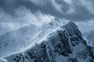 Obraz premium Dramatic snow covered mountain peak with swirling clouds and strong winds