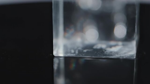 Cinematic macro shot focusing on the razor sharp edges and polished surfaces of a large glass prism moving slowly across a clean, reflective surface minimalist, Cinematic macro shot, vivid
