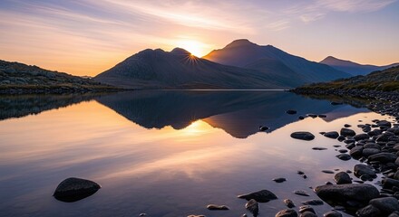 A beautiful landscape photograph of a lake reflecting the mountains and the sunset. The sky is filled with warm colors, and the water is calm. Rocks are in the