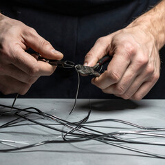 Hands using wire cutters to snip thin metal wire on a textured gray surface