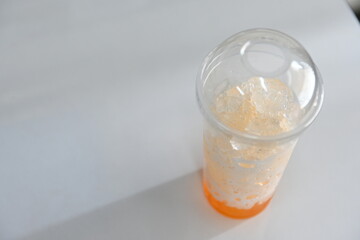 Leftover orange juice with ice in a clear plastic cup.