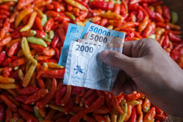 Close-up of a cash transaction using Indonesian rupiah at a traditional market, with hands exchanging money above a pile of fresh chili peppers. Perfect for themes of trade, economy, finance