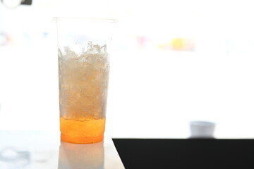 Leftover orange juice with ice in a clear plastic cup.