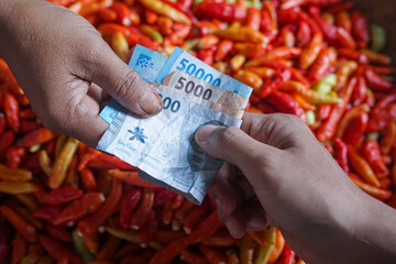 Close-up of a cash transaction using Indonesian rupiah at a traditional market, with hands exchanging money above a pile of fresh chili peppers. Perfect for themes of trade, economy, finance