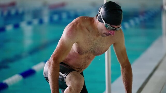 A dedicated swimmer takes a break between laps at a training session, showcasing determination and focus while wet and glistening in the pool environment.