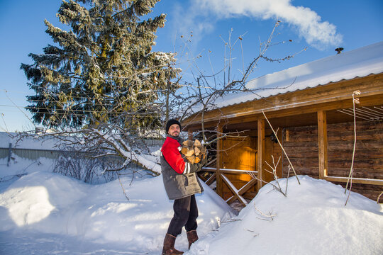 A man of European appearance heats a bathhouse with wood on a frosty sunny winter day.