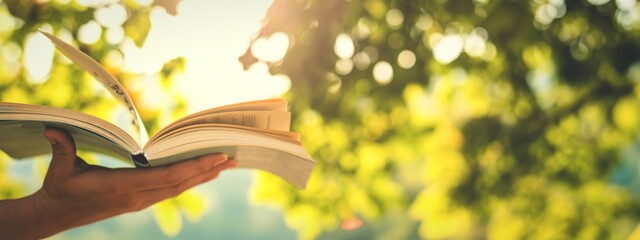 Person holding open book outdoors with dappled sunlight through leaves