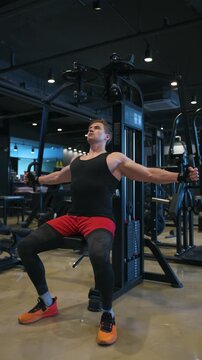 Man performing chest fly isolation on a weight machine, expanding and contracting pectoral muscles during intense strength training at a gym - vertical static shot