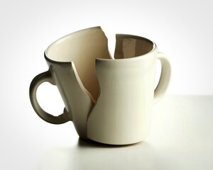 A white ceramic mug shattered into multiple pieces on a white surface