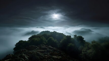 A serene and atmospheric mountain landscape shrouded in fog illuminated by a bright moon at night
