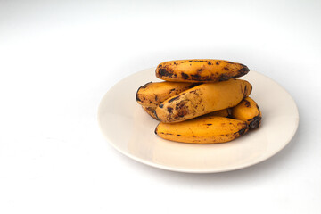 A stack of very ripe bananas (showing several brown spots/specks) served on a slightly off-white ceramic round plate.