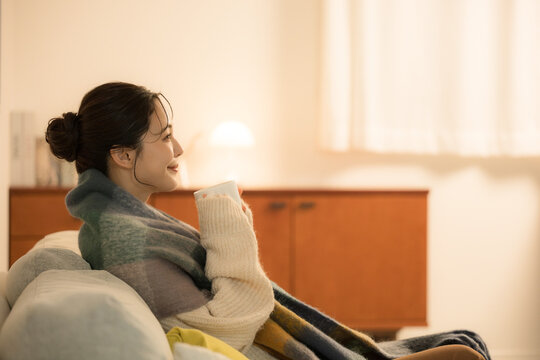 夜の灯りの部屋でホットドリンクを飲む若い女性　女性の冬イメージ　白熱灯のあたたかいイメージ