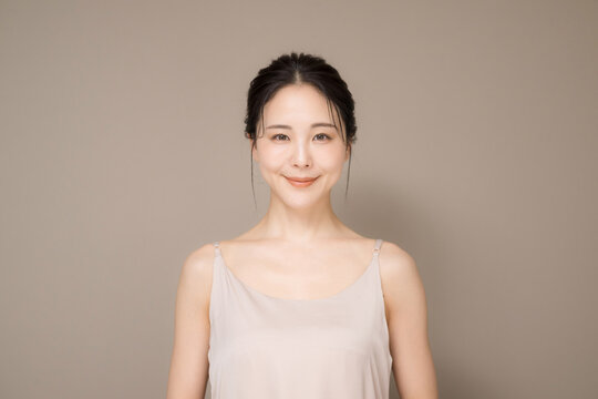 髪の毛がアップ背景がベージュの使いやすい美容やスキンケアの美しい女性のイメージ上半身正面カメラ目線