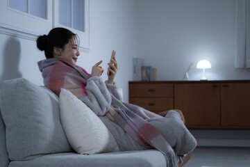 Young woman holding a smartphone in a dimly lit room at night Winter image of a woman, full body